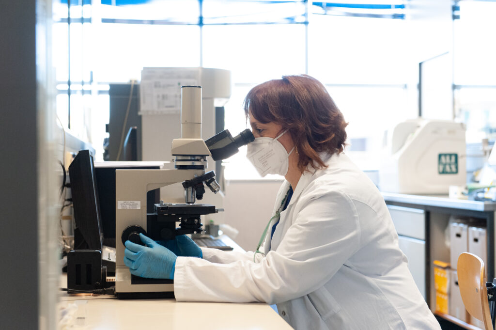 dottoressa in laboratorio che analizza campioni al microscopio con mascherina